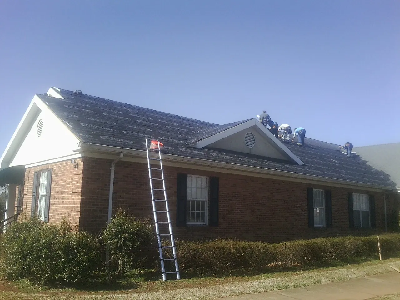 Crew tearing shingles off a brick ranch roof with a ladder set — Emergency Roof Repair work by our crew in Declo