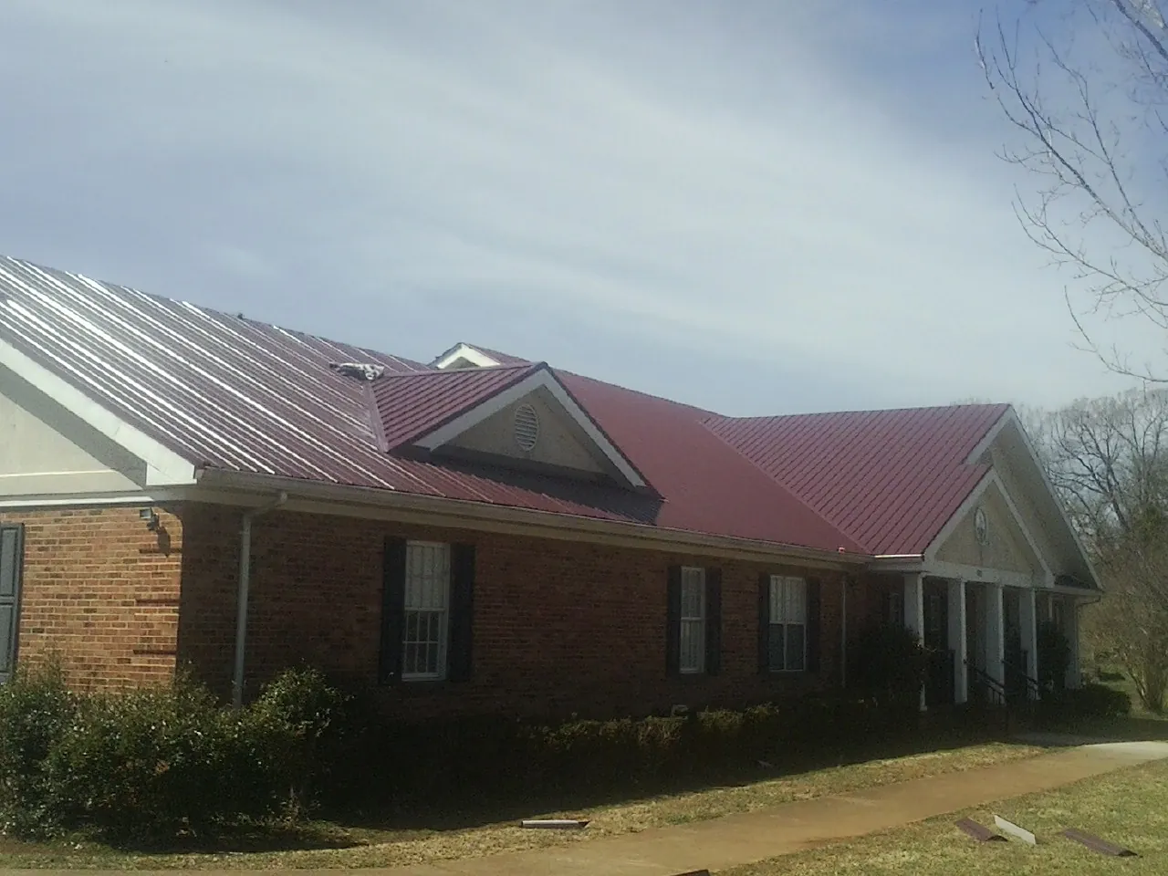 Red metal roof with gabled entries on a long brick building, from a Hail Damage Roof Repair job in Declo