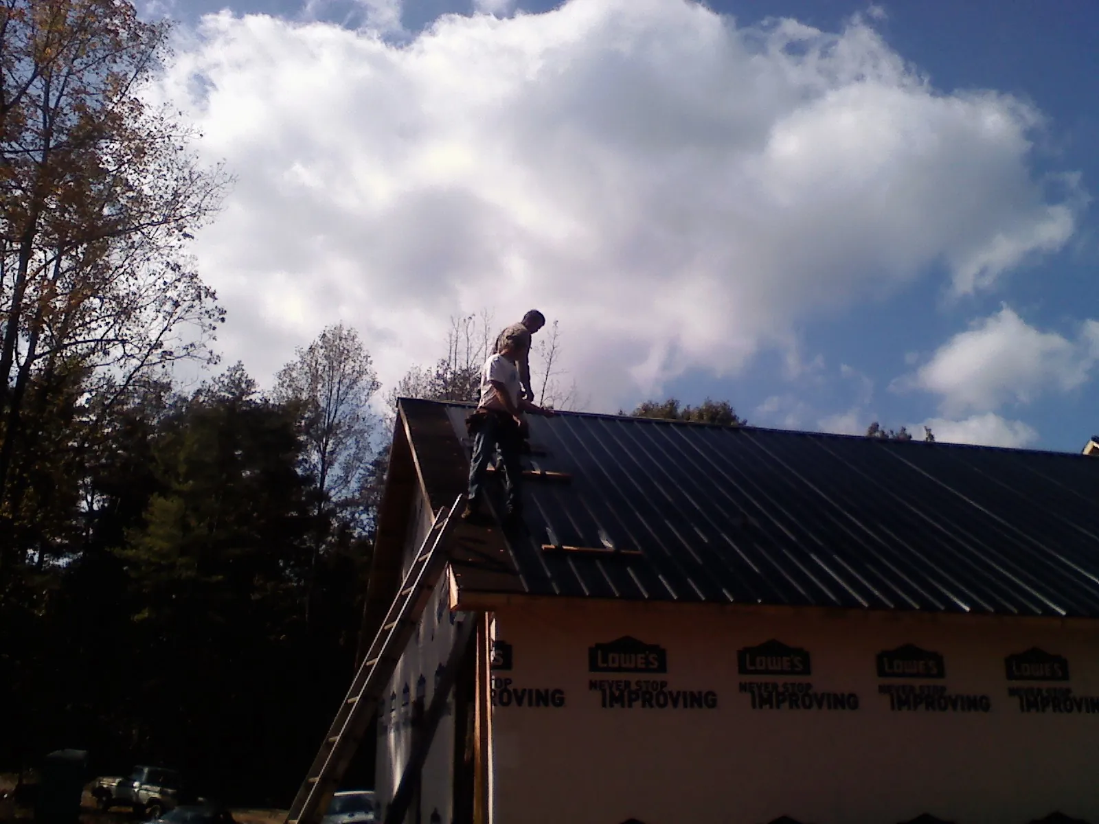 Roofer fastening dark metal panels high against a cloudy sky, from a Roof Inspection job in Declo